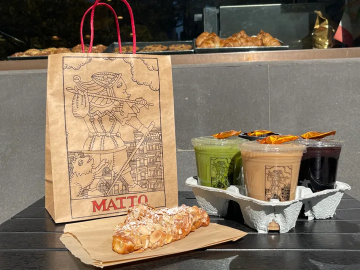 Matto takeaway drinks and an almond croissant beside a branded paper bag
